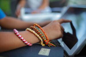 A hand of young woman with many handmade bright bracelets is touching screen of laptop to check orders at her online shop, digital small business, e-commerce of artisanal goods. Remote job